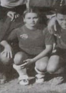 Fotografia de Valéria Sampaio, jogadora de futebol feminino e lateral da Escolinha do Flamengo, sorrindo uniformizada no campo de futebol.