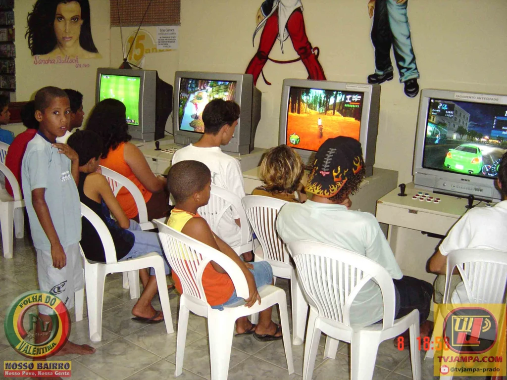 Fotografia colorida no interior da locadora Byte Games em 2003, mostrando jovens sentados em cadeiras brancas jogando videogame em televisores de tubo.