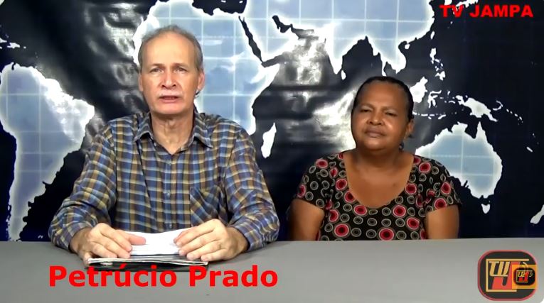 Registro digital da imagem Entrevista Maria Auxiliadora no estúdio do programa Jampa é Notícias, mostrando o apresentador Petrúcio Prado de camisa quadriculada ao lado da entrevistada Maria Auxiliadora, que veste uma blusa estampada com círculos. Ao fundo, destaca-se um painel com o mapa-múndi estilizado em tons de azul e branco e o logotipo da TV JAMPA.