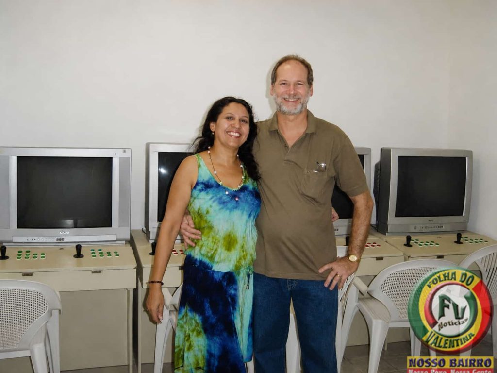 Petrúcio Prado e sua esposa Rejane Prado posam sorridentes em um espaço da Byte Games, diante de estações de jogos e computadores. A fotografia registra a união do casal e a parceria que marcou décadas de dedicação à família, ao empreendedorismo e à comunicação comunitária.
