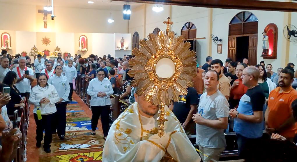 Padre José Luis segura o Ostensório dourado com o Santíssimo Sacramento diante dos fiéis na celebração de Corpus Christi no Valentina Figueiredo