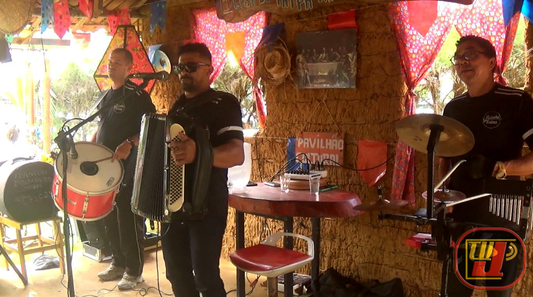 Luizinho do Forró tocando sanfona acompanhado de sua banda com zabumba e bateria no Pavilhão Cultural do Restaurante Rural Casa de Taipa, durante cobertura especial da TV JAMPA Oficial no Conde, Paraíba.
