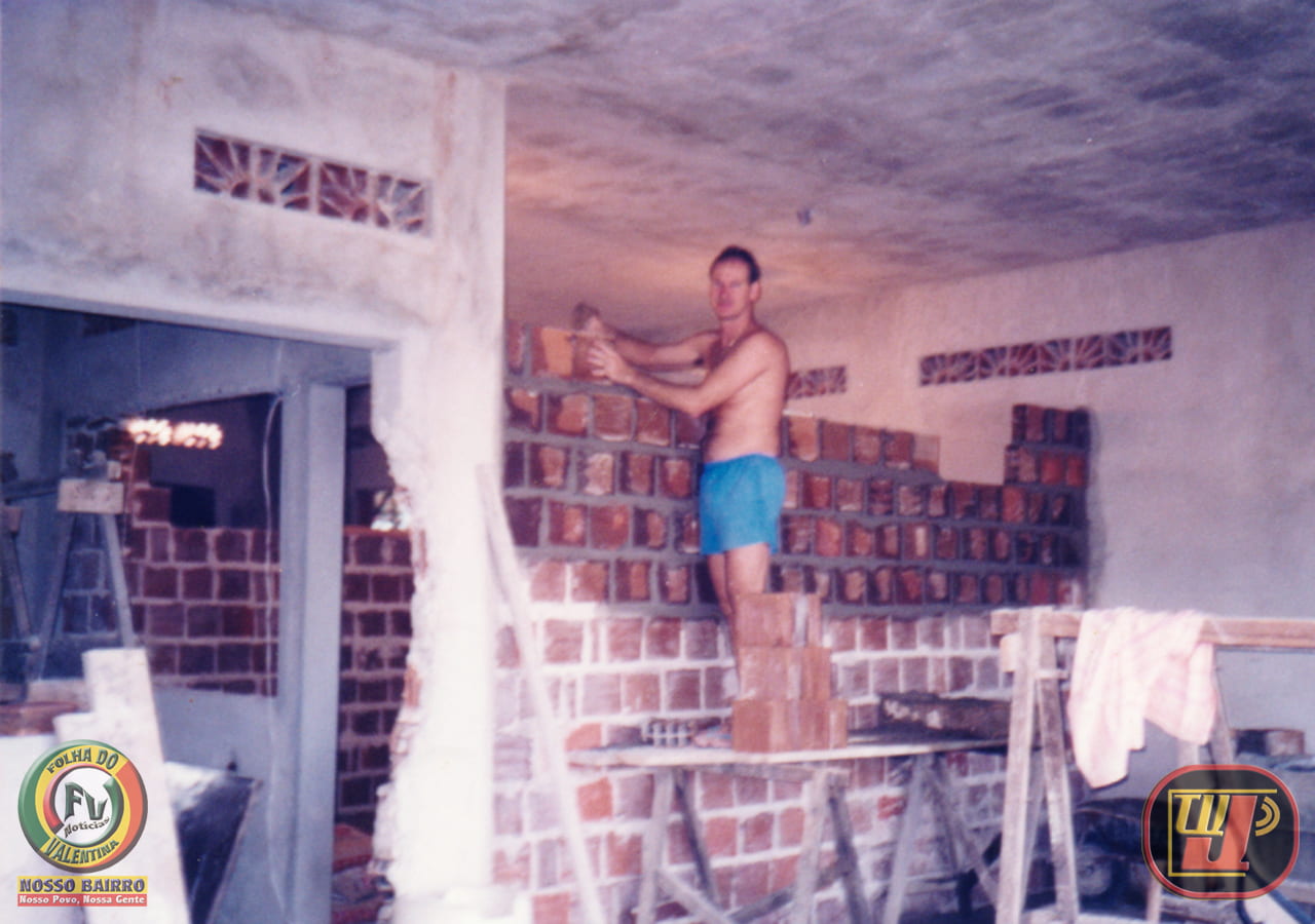 Fotografia histórica em ambiente interno mostrando Petrúcio Prado jovem, sem camisa e de bermuda azul, trabalhando ativamente na construção civil. Ele está em pé sobre uma plataforma de madeira apoiada em cavaletes, assentando tijolos cerâmicos com massa para levantar uma parede divisória interna. O ambiente está em obras, com tijolos aparentes, colunas de concreto e aberturas de ventilação na parede ao fundo. No canto inferior esquerdo consta a marca circular "Folha do Valentina Notícias / Nosso Bairro, Nosso Povo, Nossa Gente" e, no canto inferior direito, o logotipo clássico da TV Jampa.