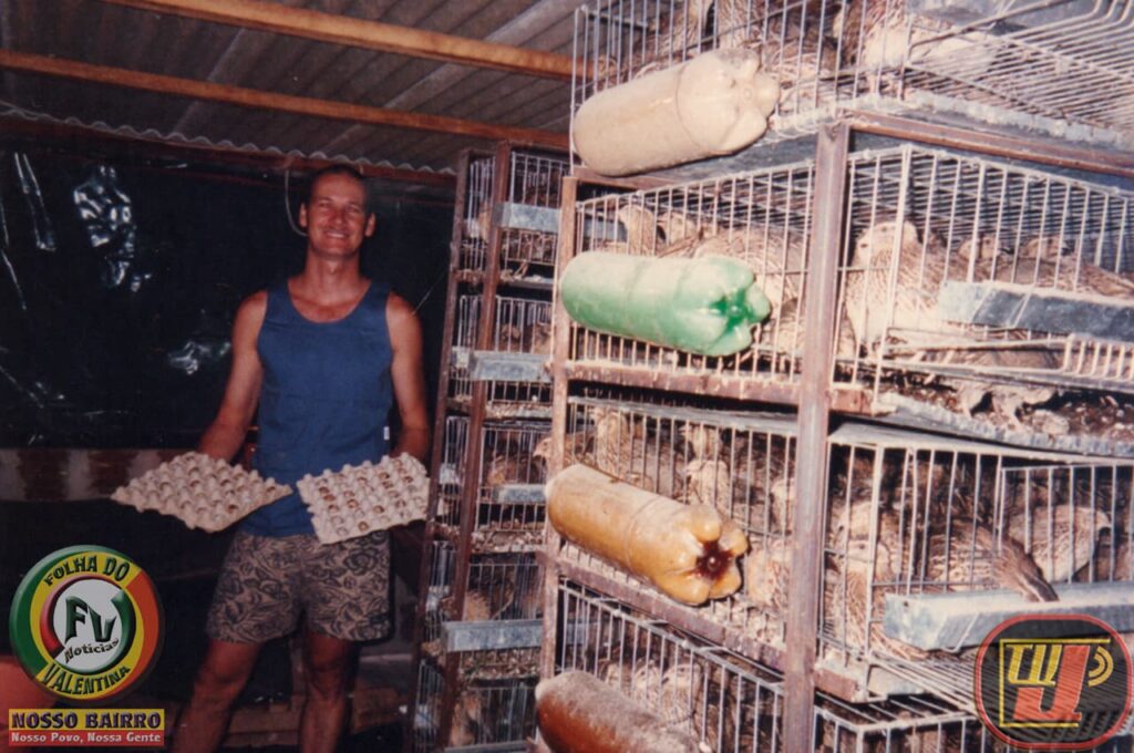 Foto colorida de um homem sorridente de regata azul e bermuda estampada, em pé dentro de um criatório de codornas. Ele está posicionado à esquerda e segura duas cartelas de ovos vazias. À direita, há uma grande estrutura vertical com várias gaiolas de metal aramadas sobrepostas, repletas de codornas. Garrafas plásticas cortadas (PET) estão fixadas na frente de cada nível da gaiola. No canto inferior esquerdo, há o logotipo redondo "Folha do Bairro Notícias - Valentina" e a frase "NOSSO BAIRRO - Nosso Povo, Nossa Gente". No canto inferior direito, aparece o logotipo estilizado "TV Jampa".