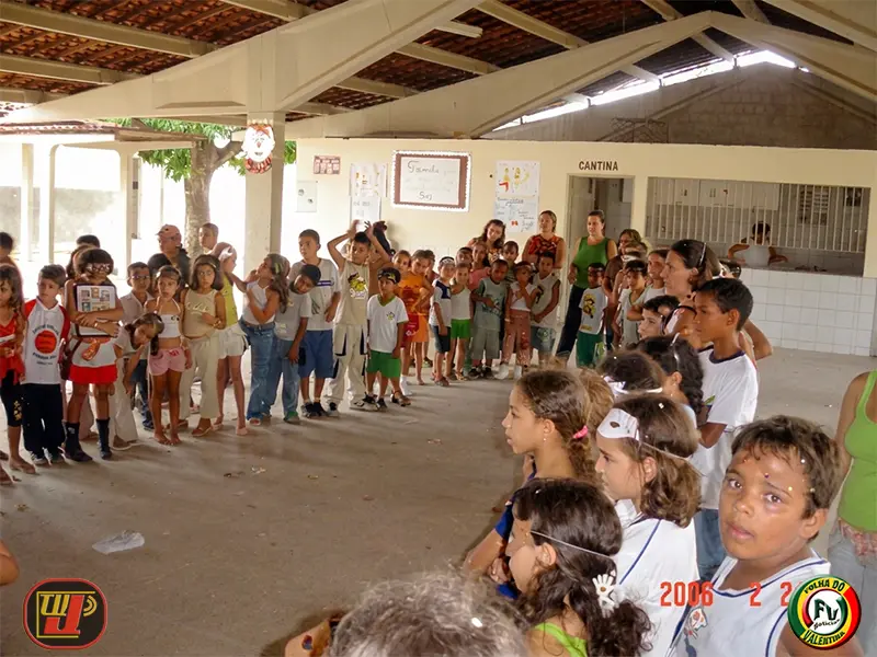 Crianças organizadas em filas e assistindo a uma atividade no pátio coberto da escola ao lado da cantina, durante o Carnaval Beneficente Dr. João Navarro.