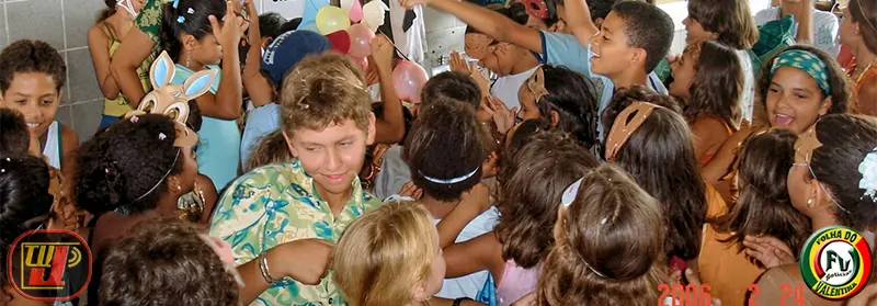 Crianças fantasiadas com máscaras e comemorando juntas em meio a balões coloridos durante as festividades do Carnaval Beneficente Dr. João Navarro.