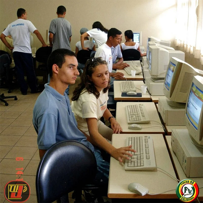 Laboratório de informática lotado de moradores utilizando computadores desktop com o auxílio de voluntários durante a ação voluntária na Fundação Bradesco.