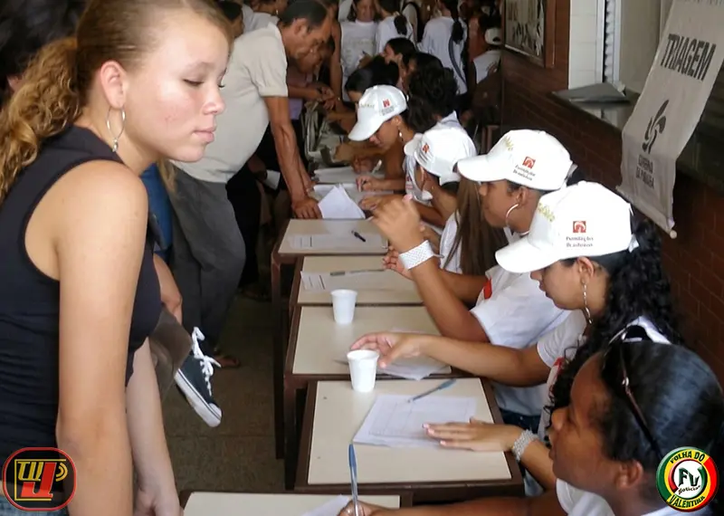 Jovens organizam fichas de triagem em mesas durante o IV Dia Nacional de Ação Voluntária Fundação Bradesco, enquanto pessoas aguardam atendimento.