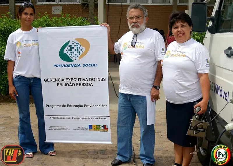 Três voluntários vestindo camisas do evento seguram um banner do INSS sobre educação previdenciária e saúde durante o IV Dia Nacional de Ação Voluntária Fundação Bradesco
