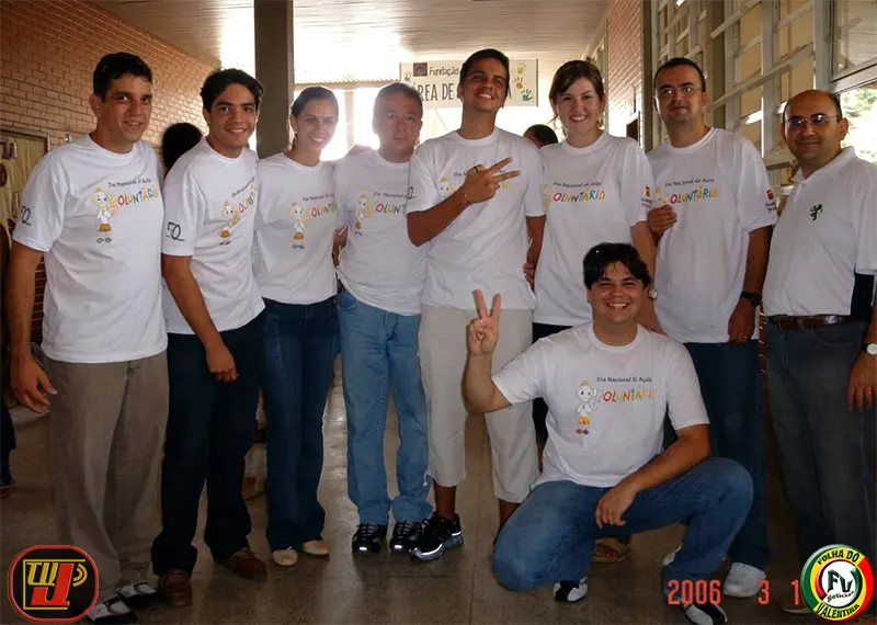 Um grupo de voluntários vestindo camisetas brancas do evento posa sorrindo em um corredor durante o IV Dia Nacional de Ação Voluntária Fundação Bradesco.